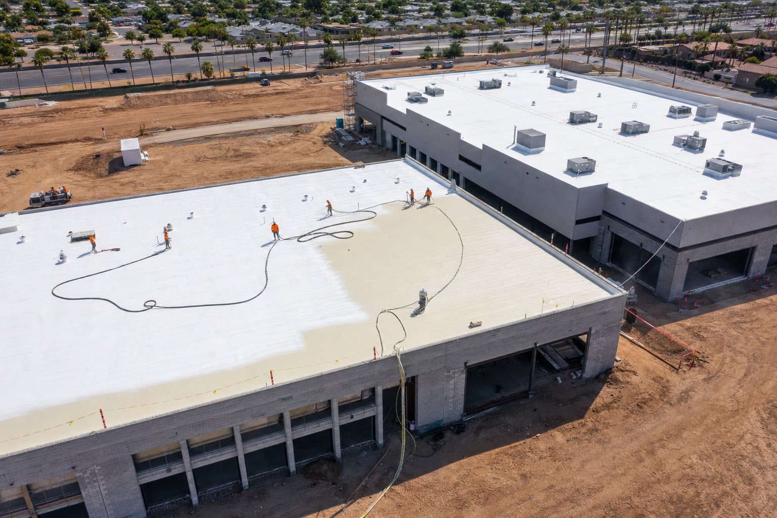 Aerial view of new construction commercial building in Phoenix with roofers spraying fresh foam roof and adjacent completed building