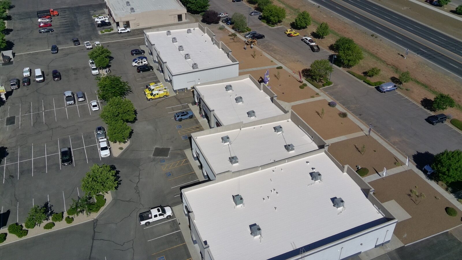 Aerial drone view of the completed 24,000 sq ft 2nd Street Plaza retail center in Prescott Arizona with tan silicone recoating, framed by the highway and high desert backdrop