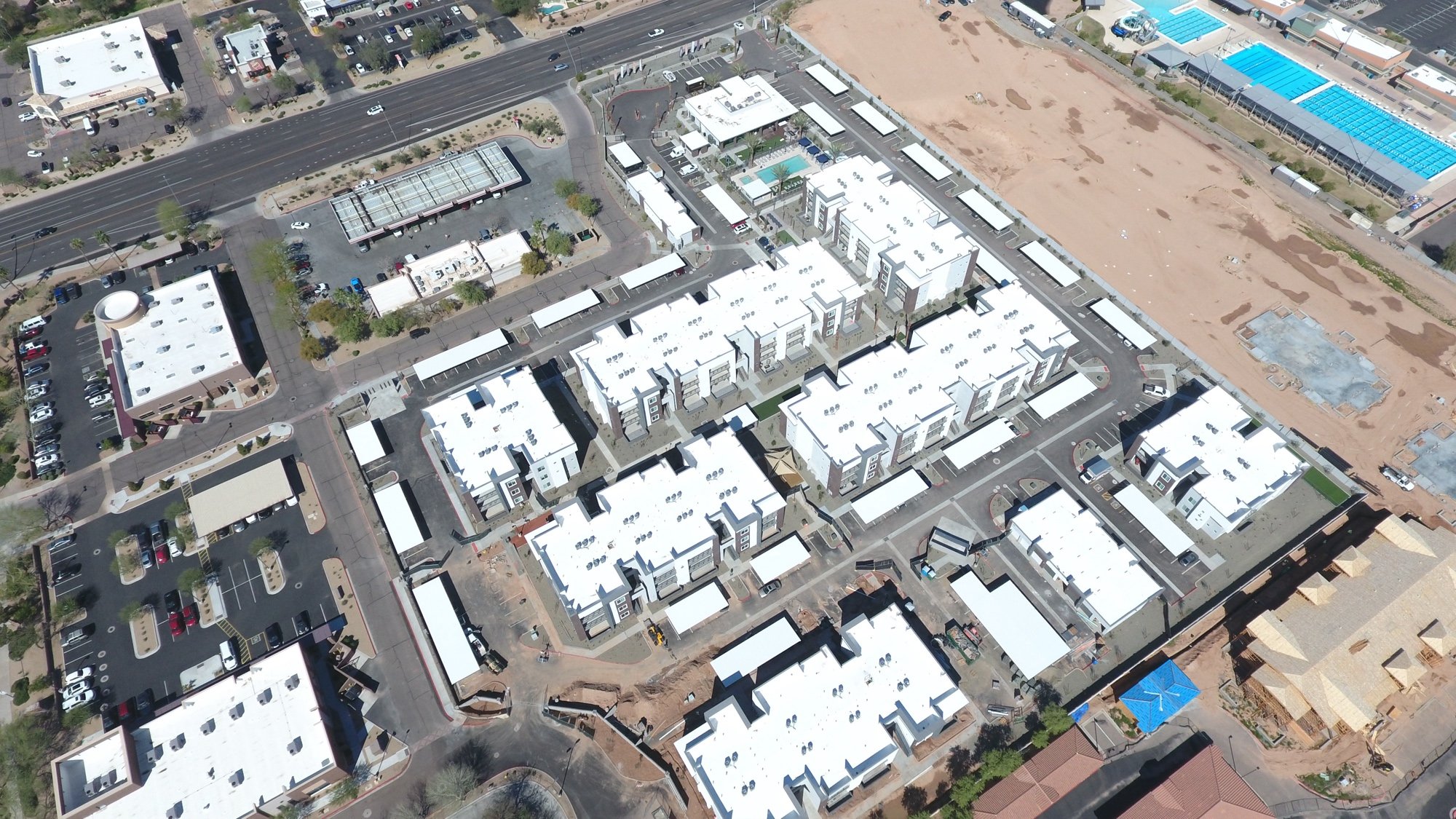 Completed aerial view of the Aster at Mountain Vista multifamily community in east Mesa AZ showing all 11 buildings with finished polyurethane foam roofs coated in bright white ARMORCOAT AC100 — Superstition Mountains visible in the distance