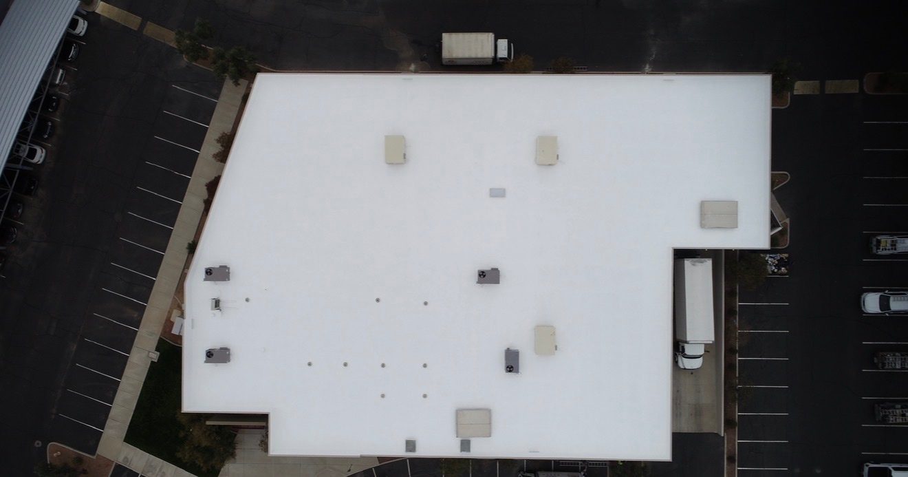 Top-down aerial drone view of the AV Dimensions Chandler industrial building after foam recoat showing the completed reflective white AC100 elastomeric coating with sealed penetrations and HVAC curbs