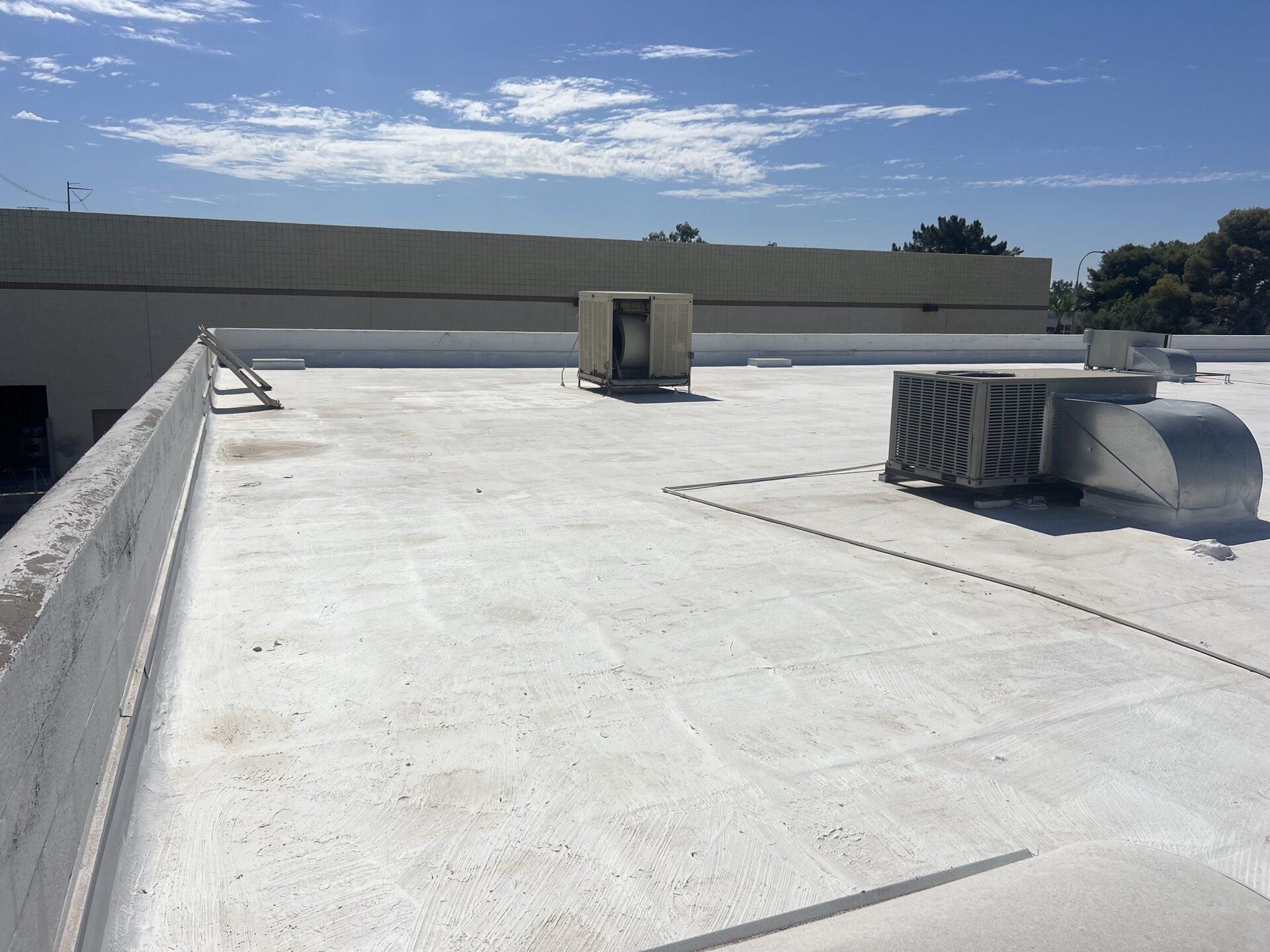 Ground-level view of the completed 9,820 sq ft new spray polyurethane foam roof at 42 W Boxelder Pl in Chandler AZ finished bright white with two coats of ARMORCOAT AC100 elastomeric coating, rooftop HVAC unit and parapet wall detail visible against a clear Arizona sky