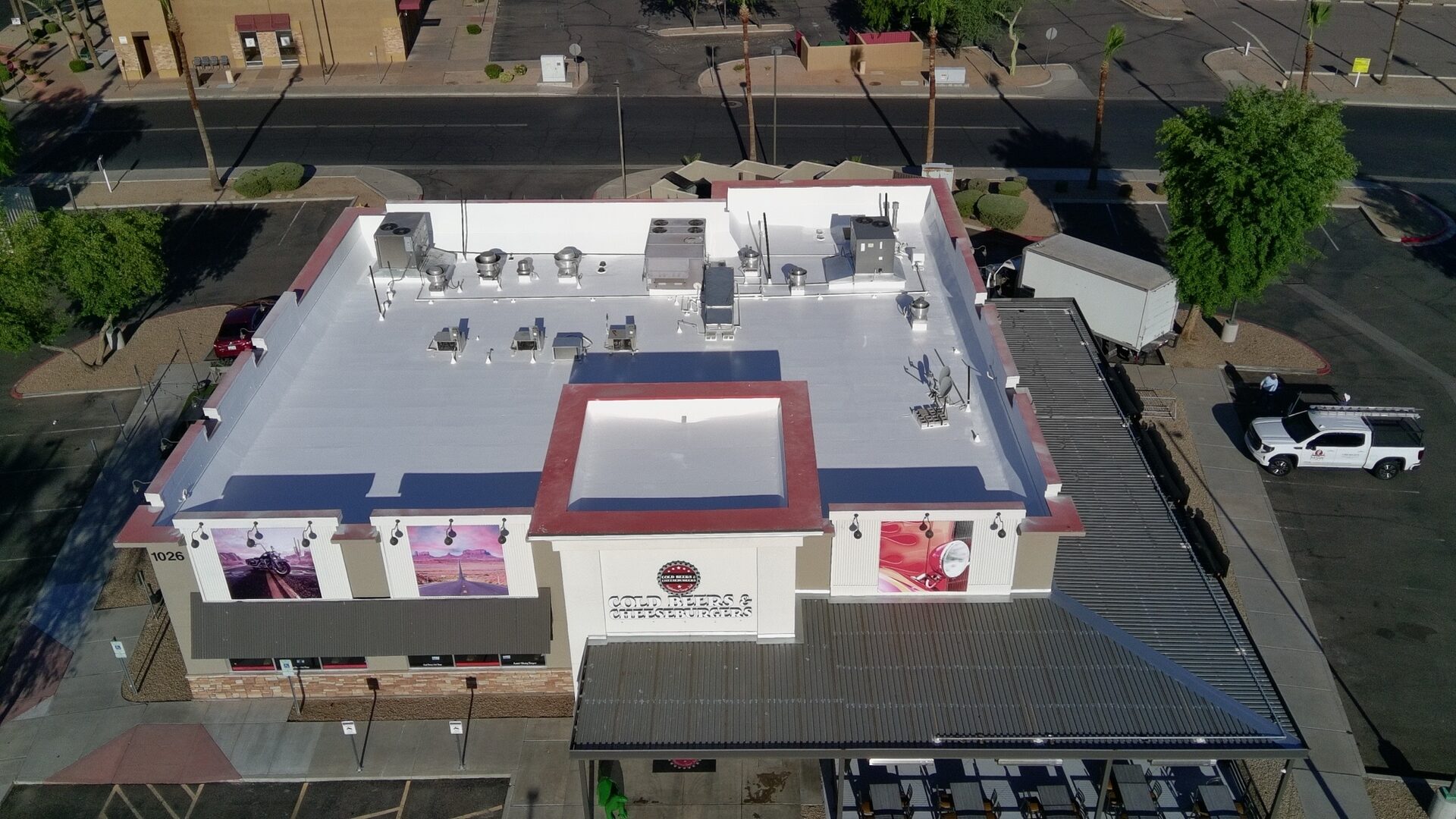 Aerial drone view of the completed Cold Beers & Cheeseburgers restaurant at 1026 S Gilbert Rd in Gilbert AZ — freshly coated bright white ARMORCOAT AC100 TPO roof framed by the signature red-painted parapet caps, with the Cold Beers & Cheeseburgers signage and branded facade art panels visible from Gilbert Road below