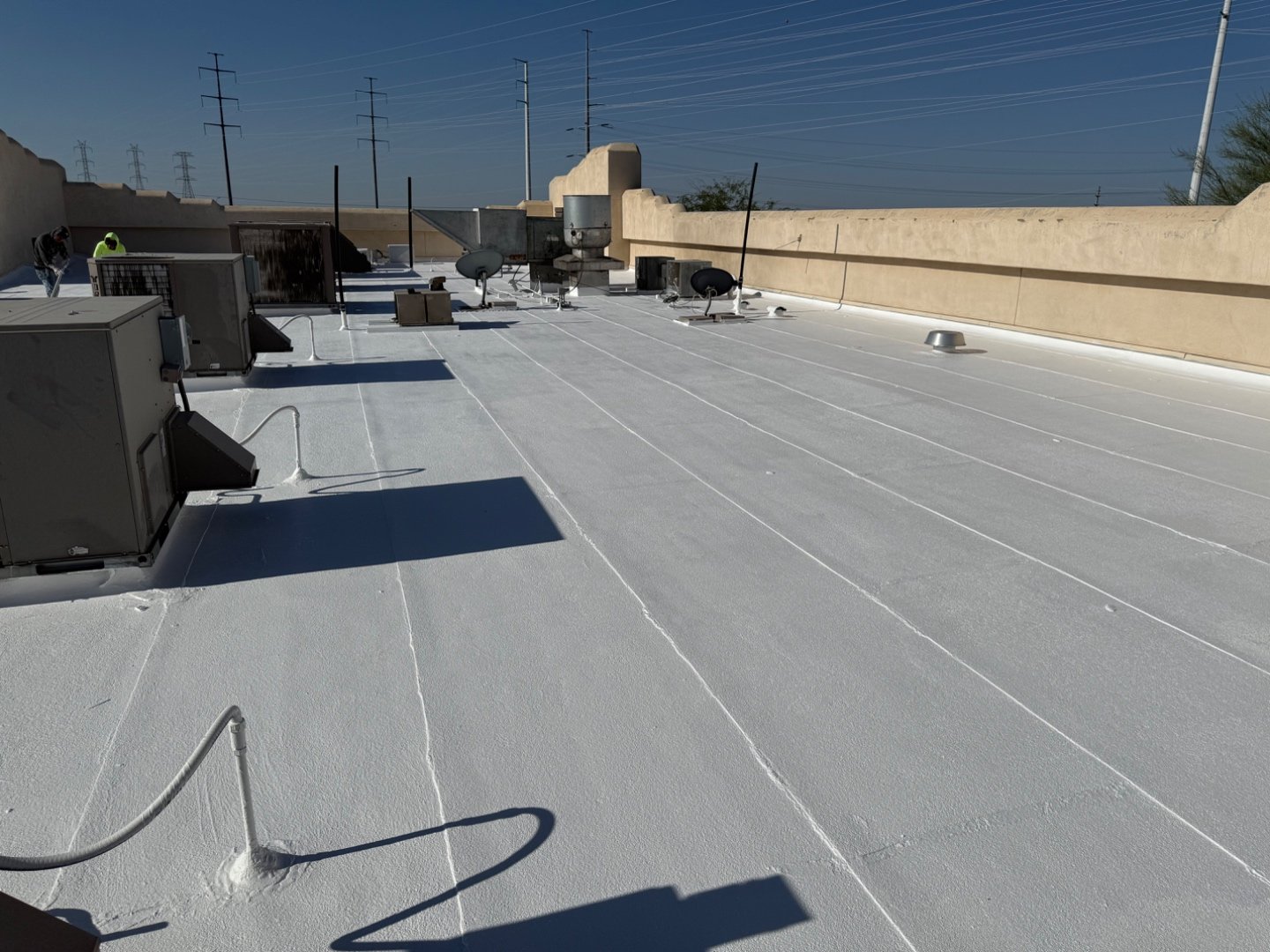 Completed foam roof restoration at Cold Beers Scottsdale — bright white TRC silicone coating, stucco parapet, HVAC penetrations, satellite dishes, crew visible on far edge