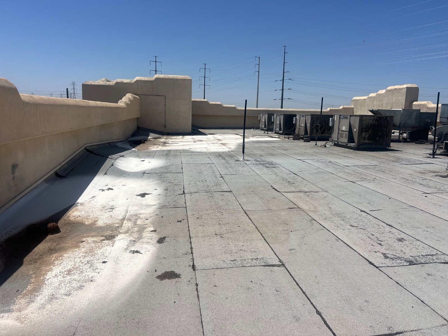Failed elastomeric coating flaking off foam roof at parapet wall, exposed foam substrate visible, cracks and dust patches