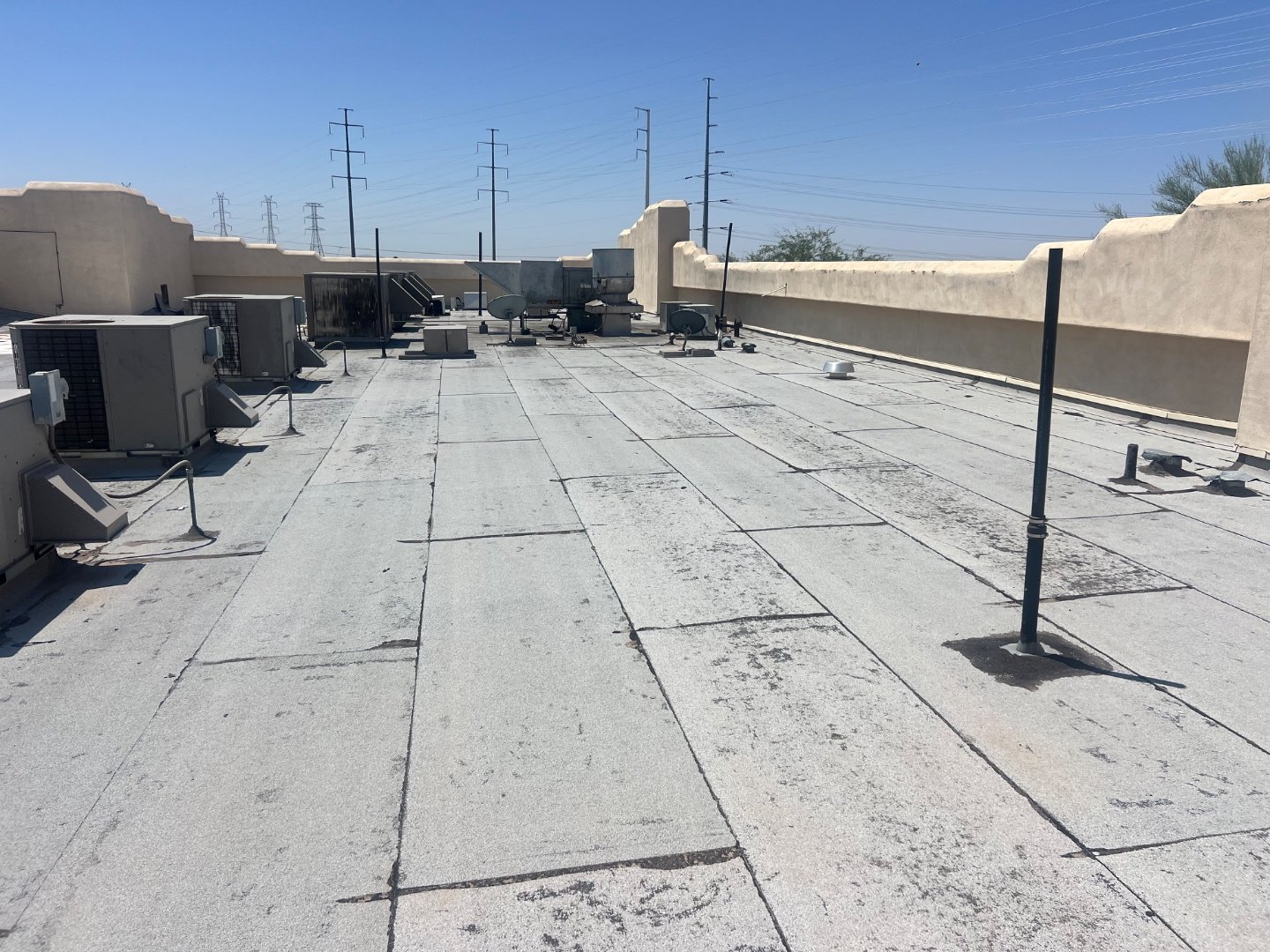 Worn foam roof surface at Cold Beers Scottsdale before restoration — chalked-out coating, hairline cracks along seams, tan stucco parapet, powerlines and desert horizon in background