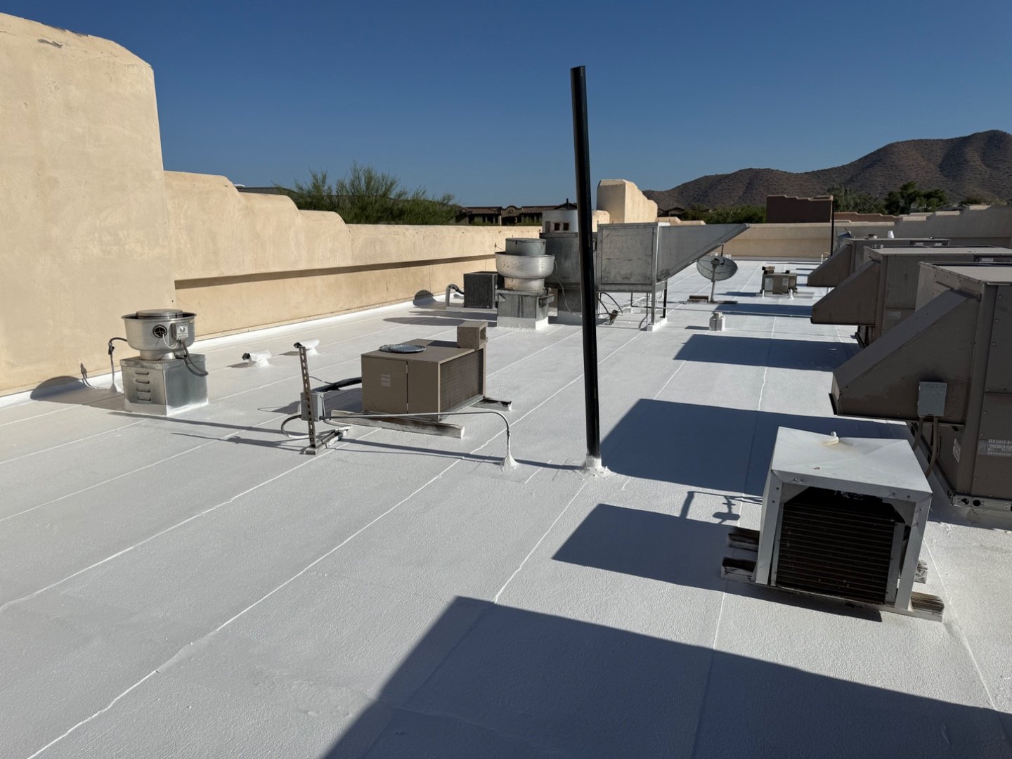 Vanguard Roofing crew in high-vis applying TRC silicone topcoat by roller on foam roof at Cold Beers Scottsdale, McDowell Mountains in background