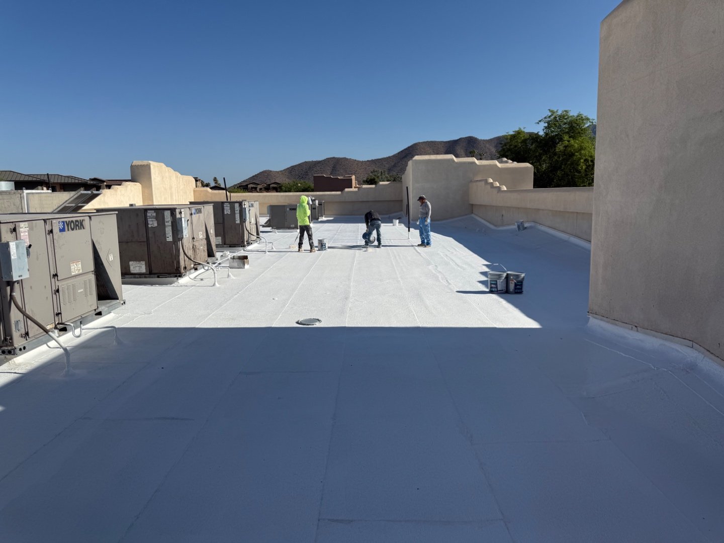 Wet-versus-cured silicone shadow line on foam roof, freshly rolled TRC white silicone next to already-set base coat, York HVAC condensers around perimeter