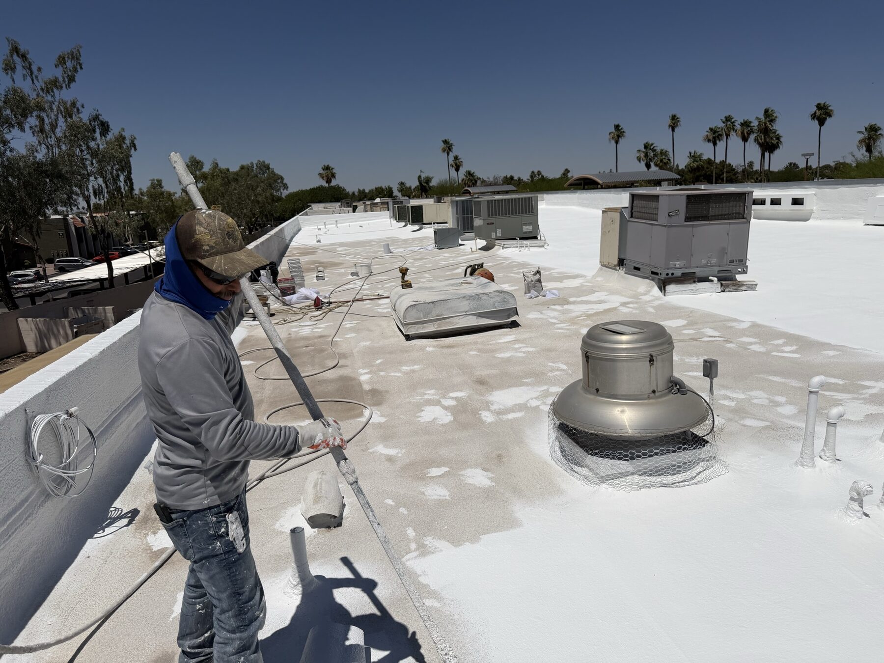 Vanguard Roofing AZ crew member applying ARMORCOAT AC100 white elastomeric coating with a spray rig on the Glendale strip mall roof restoration project
