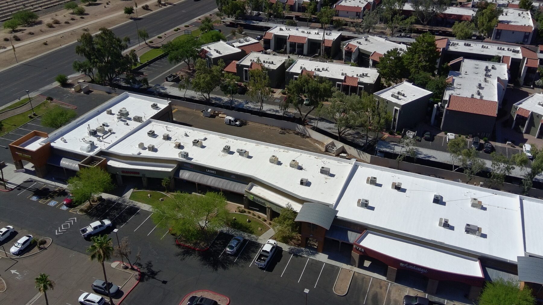 Aerial view showing tenant storefronts and the completed bright white reflective foam roof restoration at the Glendale Arizona strip mall