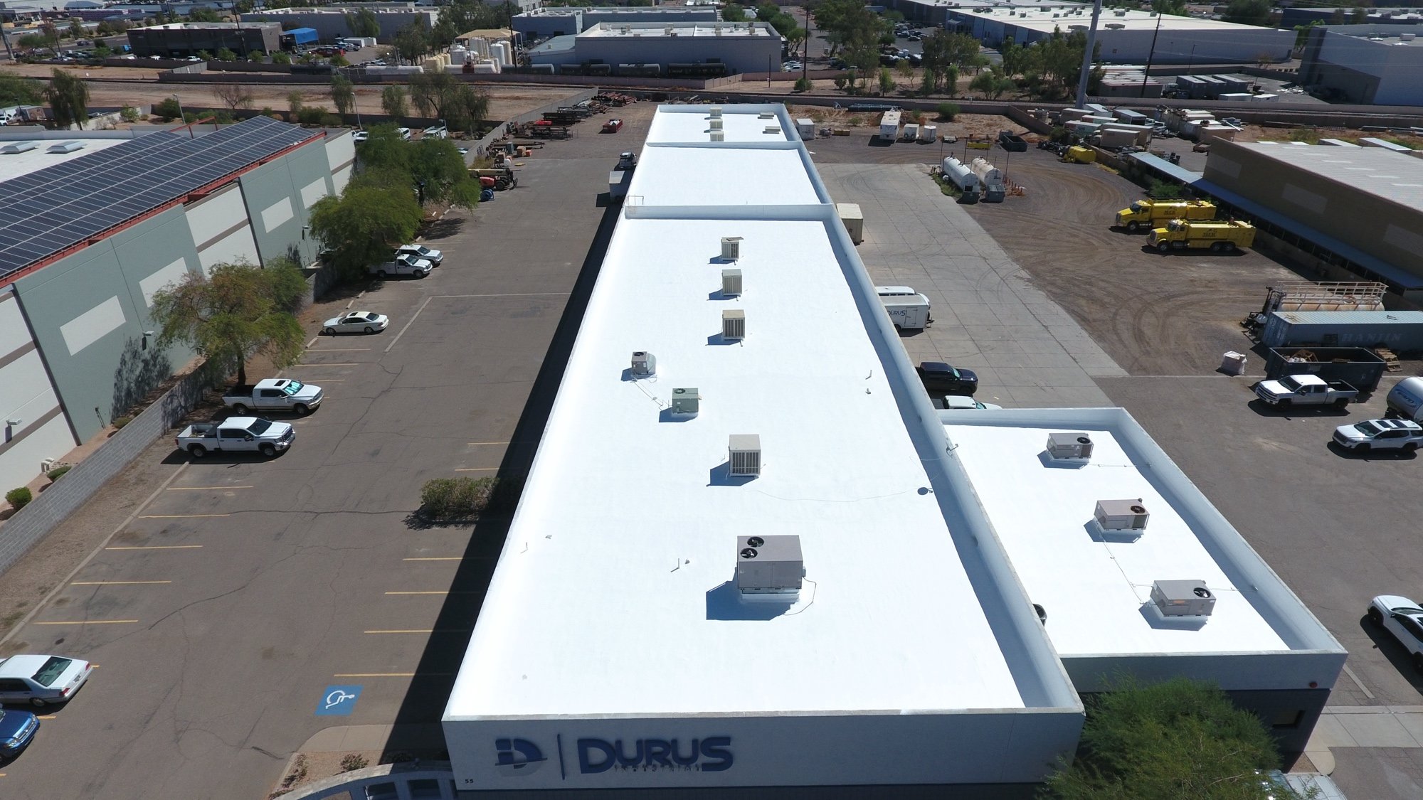 Completed drone aerial view of the finished 23,000 sq ft foam roof at Durus Industrial in Chandler AZ with the DURUS signage on the building visible from above — bright white ARMORCOAT AC100 finish covering the industrial facility