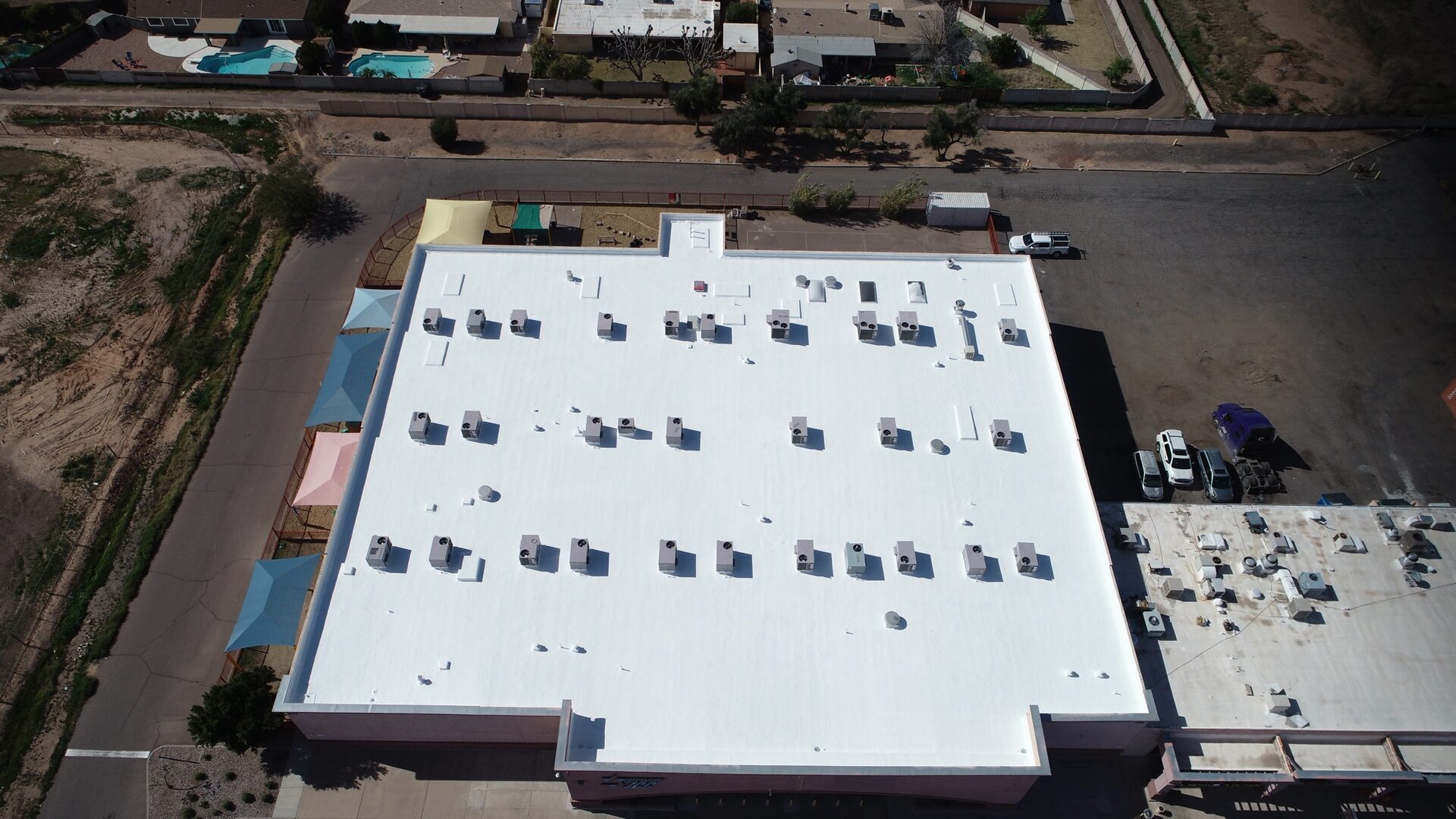 Completed 27,000 sq ft polyurethane foam roof with 2 coats of ARMORCOAT AC100 white elastomeric at East Valley Jewish Community Center on N Alma School Rd in Chandler AZ, with childrens play-area shade sails visible on the west side