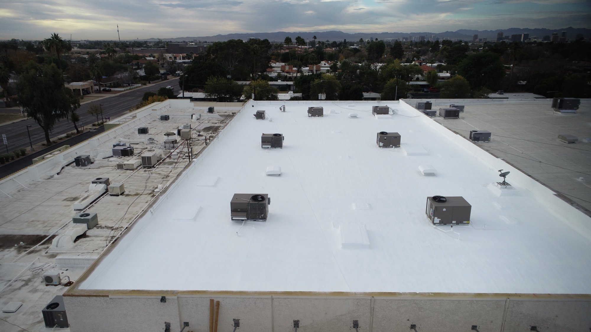 Completed foam roof at the Goodwill retail store on Bethany Home Rd in central Phoenix with the downtown Phoenix skyline visible in the background — bright white ARMORCOAT AC100 finish after the 40 foot by 190 foot tapered cricket drainage rebuild