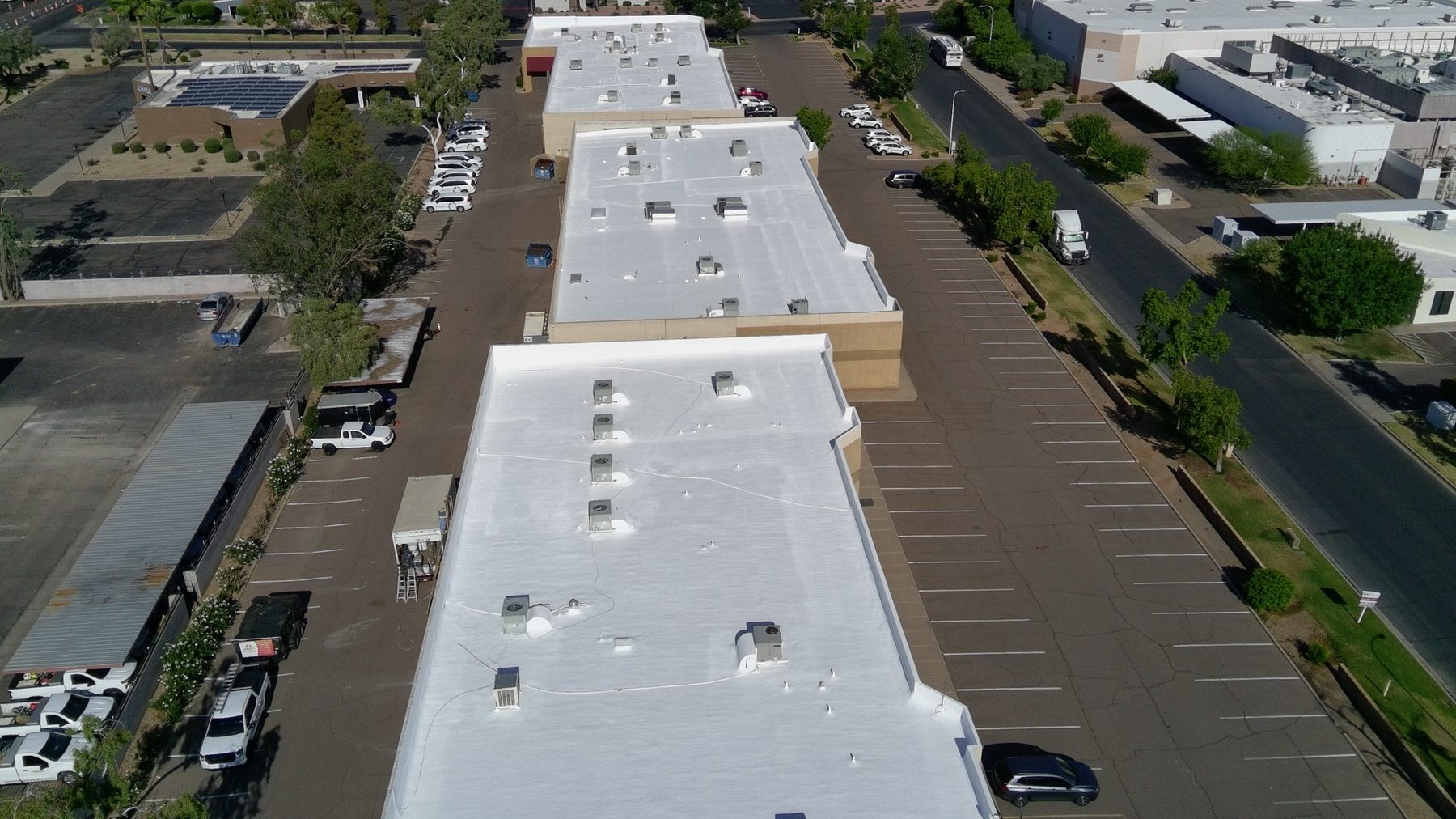 Aerial drone view of the three completed Huntington Dr commercial buildings at 2403, 2425 and 2525 W Huntington Dr in Tempe AZ — all three flex-industrial roofs finished bright white with two coats of ARMORCOAT AC100 elastomeric coating over the repaired spray polyurethane foam roofs, framed by the industrial corridor and parking lots on either side