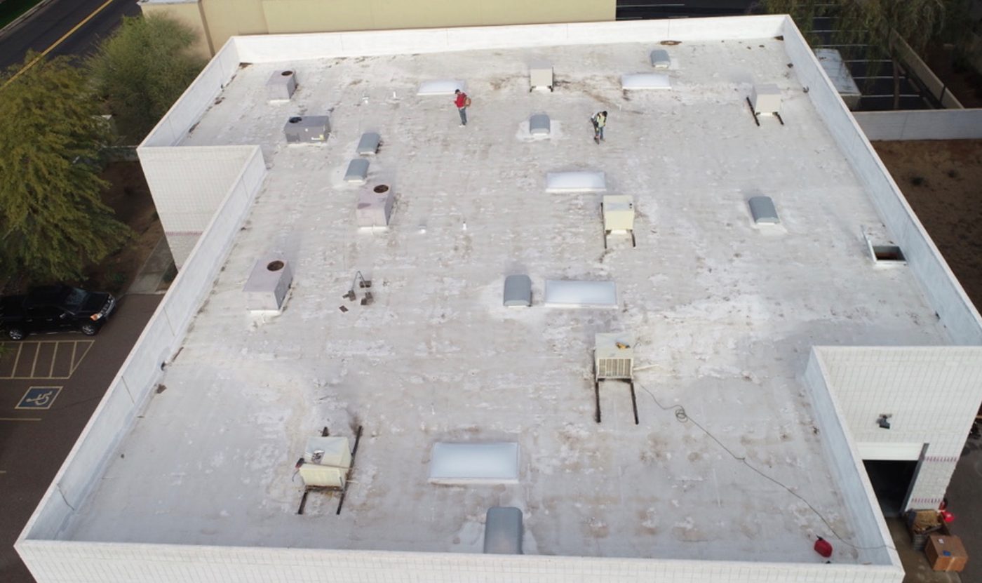 Before restoration: aerial drone photo of the aging foam roof in Chandler AZ with Vanguard Roofing crew starting prep work, showing weathered surface, HVAC penetrations, and skylight openings