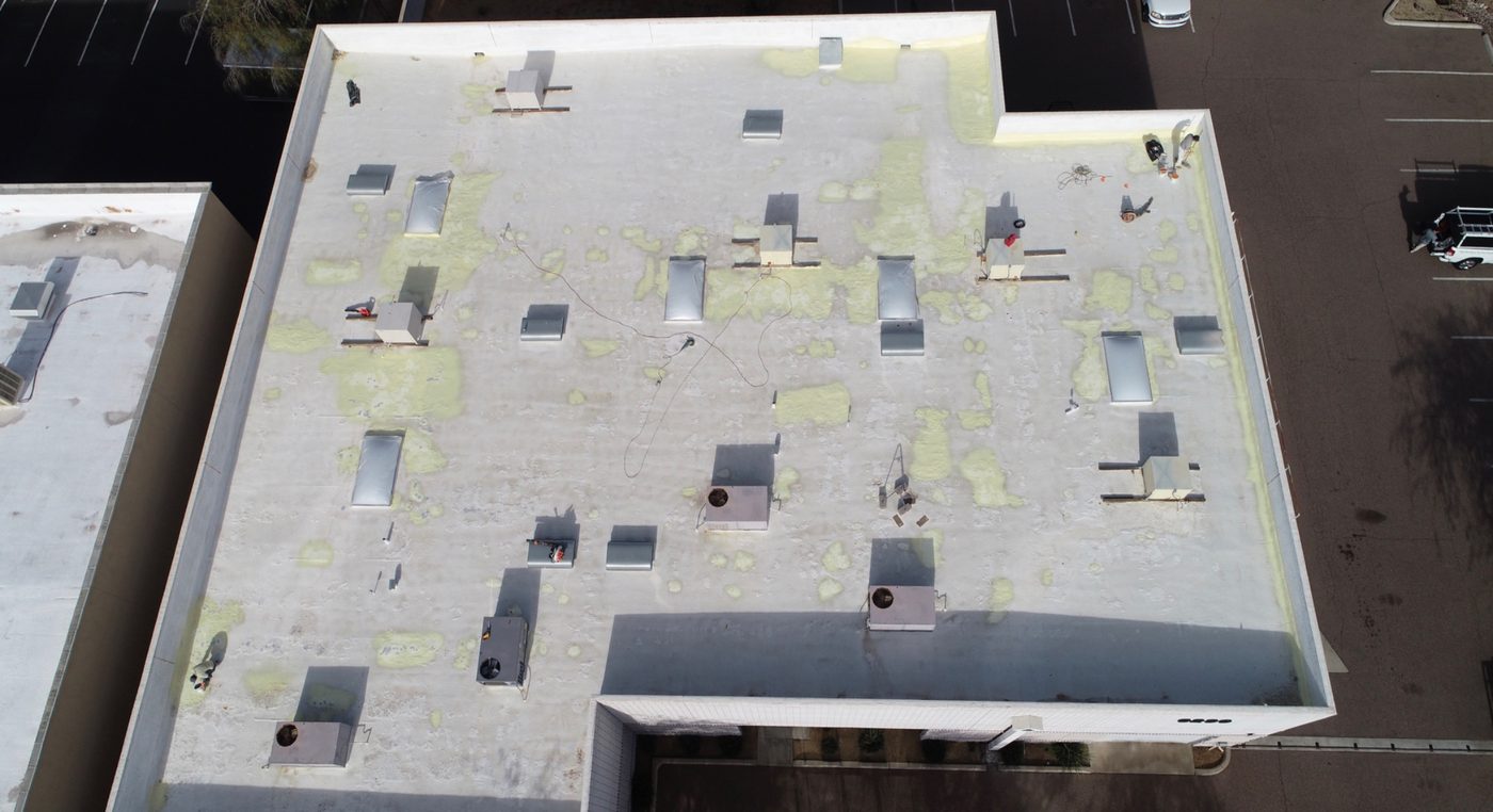 During the job: top-down aerial drone view of the 9,000 sq ft Chandler industrial foam roof showing extensive foam repair patches across the field before the AC100 elastomeric topcoat was applied