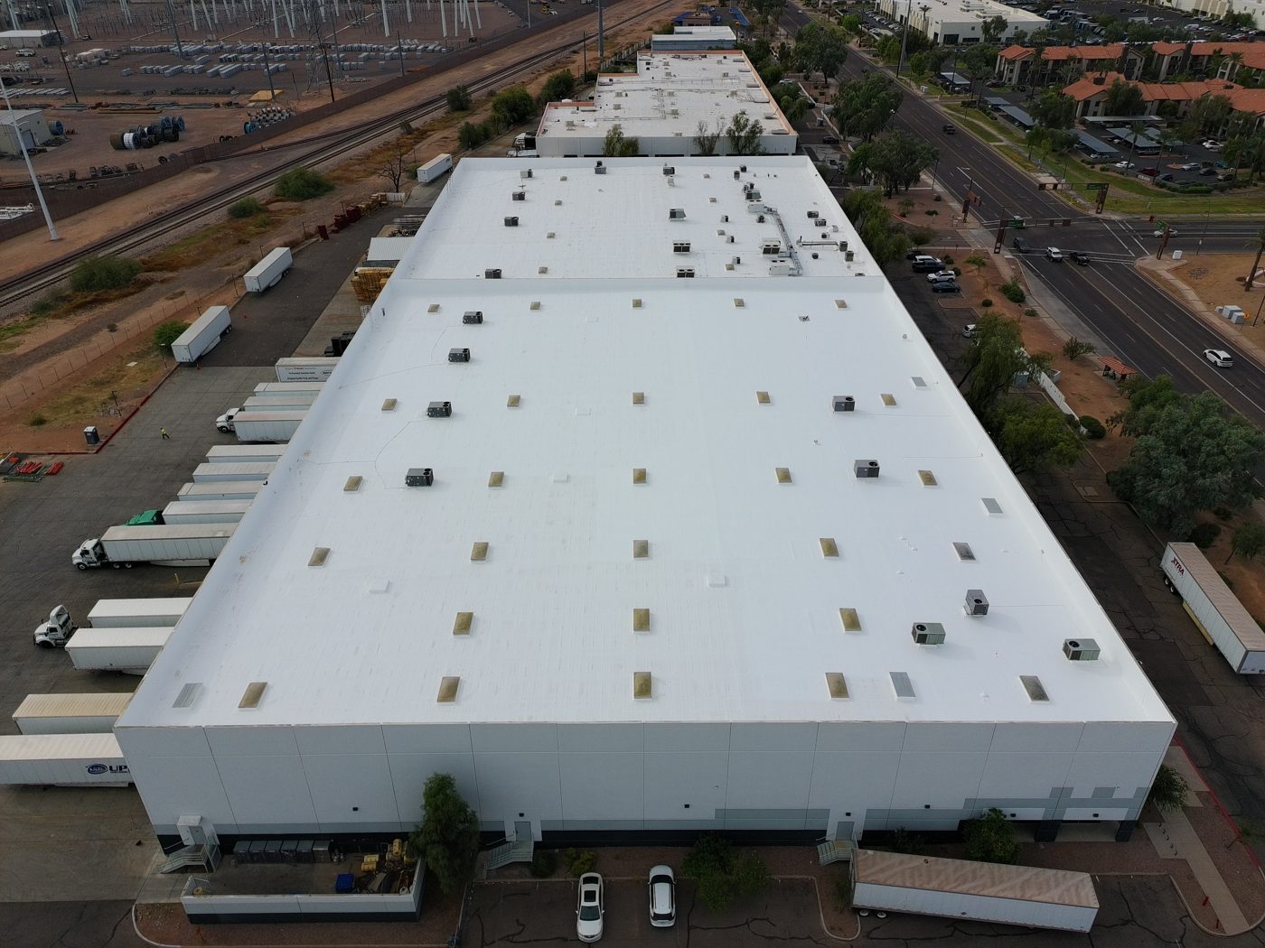After restoration: full aerial drone view of the completed 125,000 sq ft Tempe industrial warehouse foam roof with a bright white ARMORCOAT AC100 coating, skylights, rooftop HVAC units, and truck docks