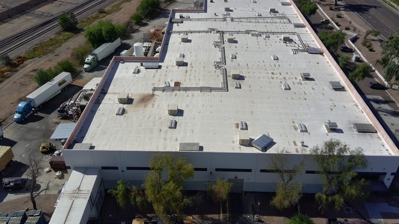 Before restoration: aerial drone view of the Tempe industrial warehouse foam roof showing a failing, dirty coating, staining, and weathered foam around skylights and rooftop equipment