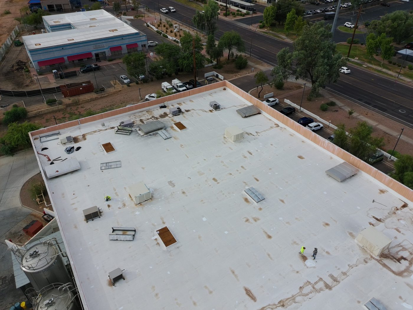 Before restoration: aerial drone photo of a section of the Tempe warehouse foam roof with Vanguard Roofing crew working leak areas, stained foam, and open rooftop equipment