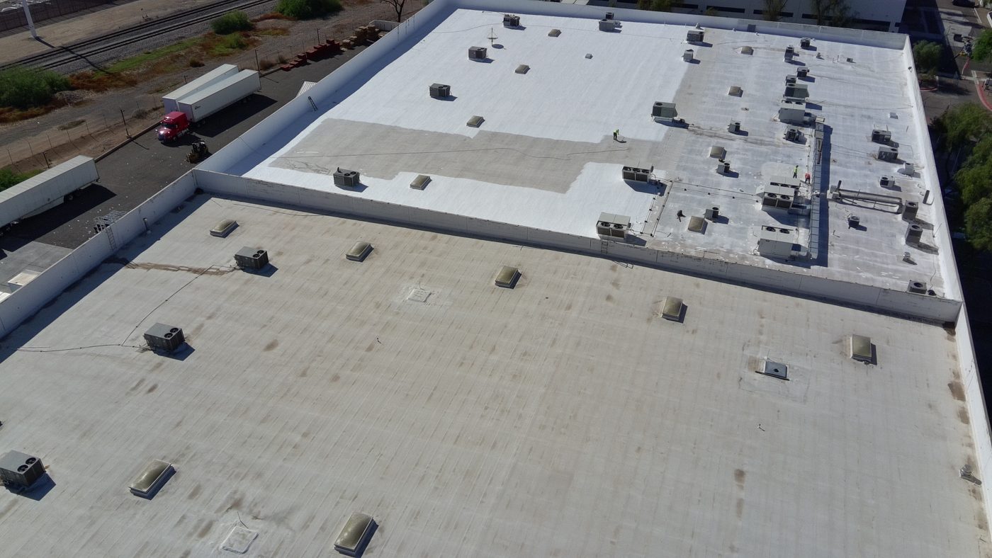 During the job: aerial drone photo of the Tempe warehouse showing a section of new white AC100 coating next to a lower roof section with the original weathered foam surface
