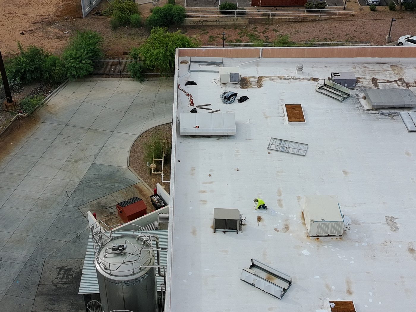 During the job: close-up aerial view of a Vanguard Roofing crew member making foam repairs on the Tempe warehouse roof near rooftop HVAC units and open equipment panels