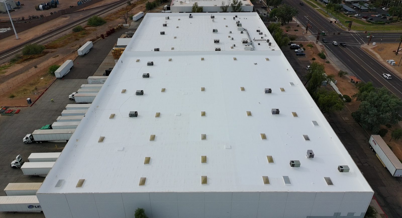 Aerial drone view of the completed 125,000 sq ft industrial warehouse foam roof in Tempe AZ with a bright white ARMORCOAT AC100 coating, skylights, and rooftop HVAC units