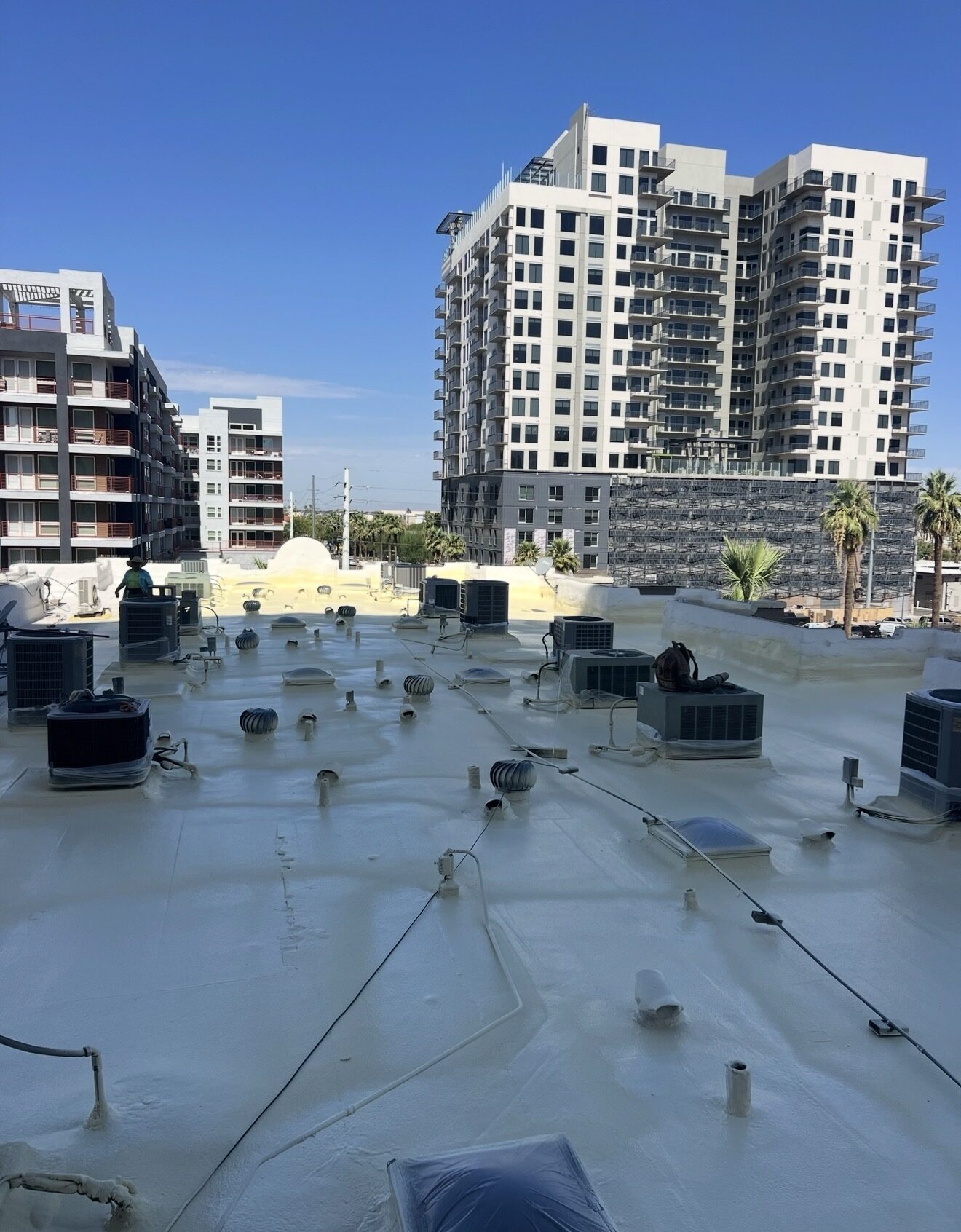 Completed white ARMORCOAT AC100 elastomeric coating on the Lofts on Fillmore HOA roof in downtown Phoenix with high-rise tower in the background and crew member in the distance