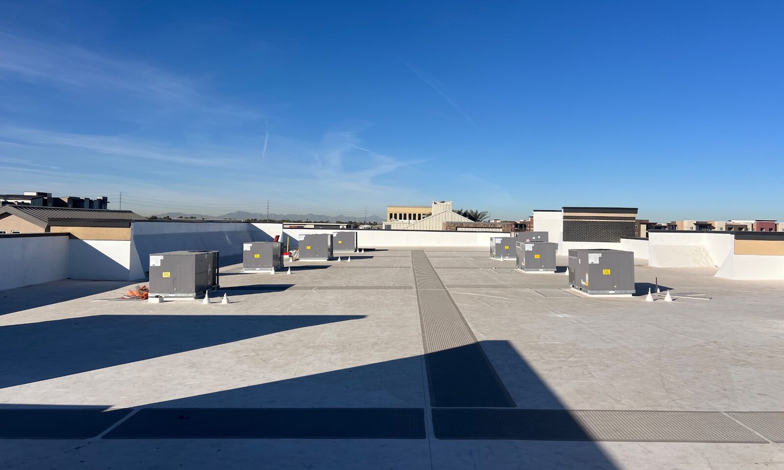 Completed 60-mil GAF TPO roof at Verde at Cooley Station retail center in Gilbert Arizona — white TPO membrane with HVAC package units, walk pads, and Phoenix mountain skyline